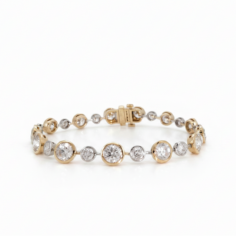 A yellow gold tennis bracelet featuring alternating round yellow gold bezel settings and round clear gemstones, photographed on a seamless white background.