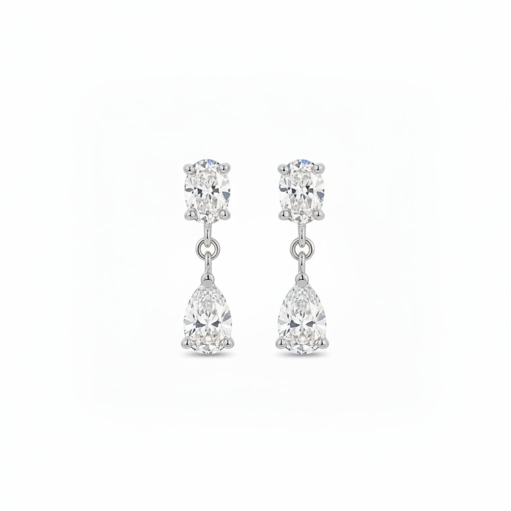A pair of white gold drop earrings featuring a oval-cut lab grown diamonds in a prong setting on the top and a pear-cut clear gemstone in a prong setting below, shown against a plain white background.
