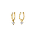A pair of yellow gold huggie hoop earrings with a small clear gemstone dangling from the bottom, set against a plain white background.