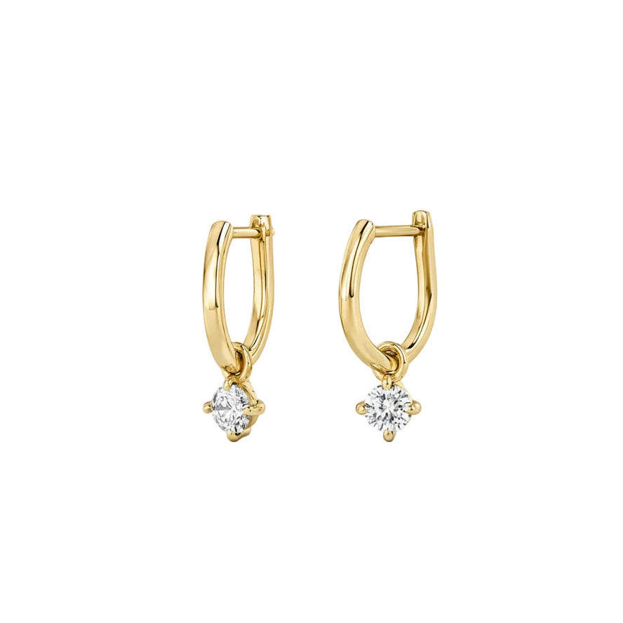 A pair of yellow gold huggie hoop earrings with a small clear gemstone dangling from the bottom, set against a plain white background.