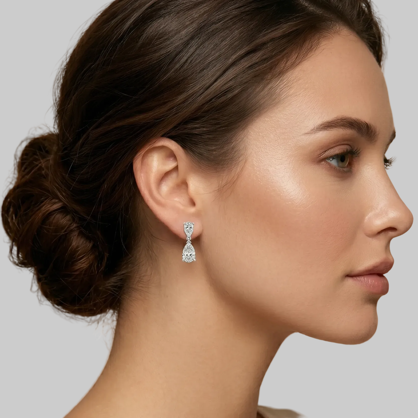 A pair of white gold drop earrings featuring two pear-cut diamonds shown on the model.