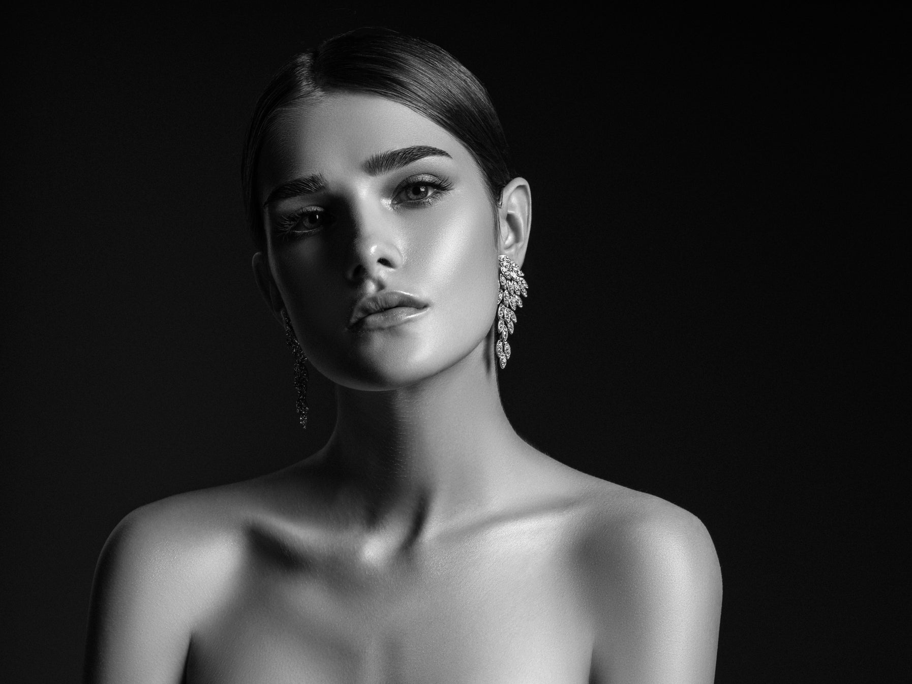 Black and white portrait of a woman wearing earrings against a dark background