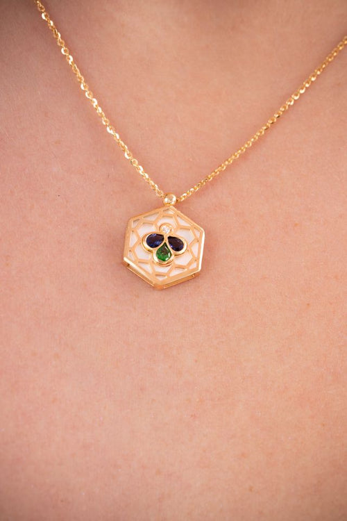 A gold chain necklace with a hexagonal pendant featuring a white center, a small clear stone, and a three-stone clover motif in blue, green, and gold on a model.