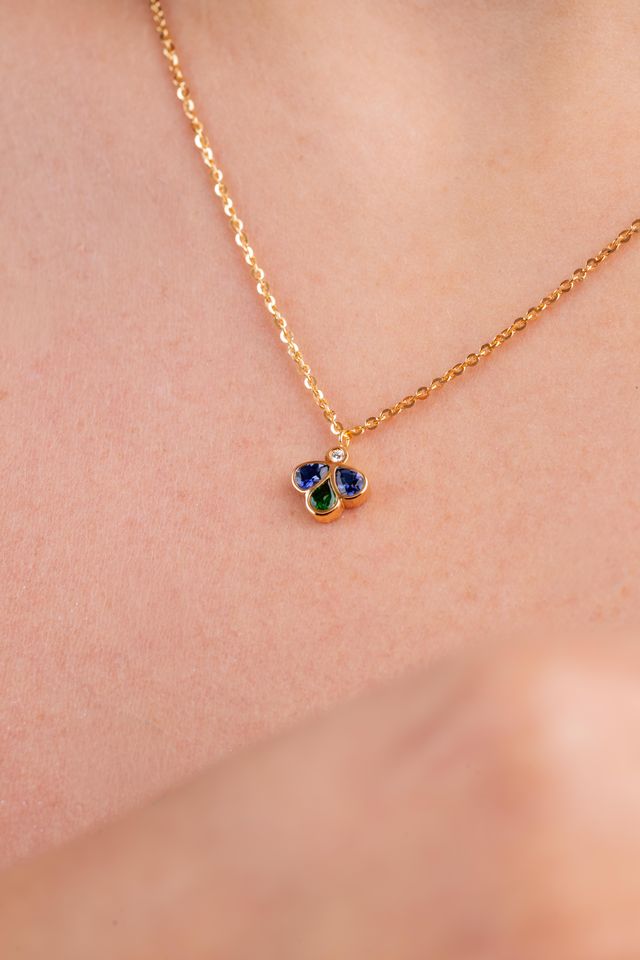 A delicate gold chain necklace with a small three-stone pendant featuring blue, green, and gold accents, shown worn on a person's neck.
