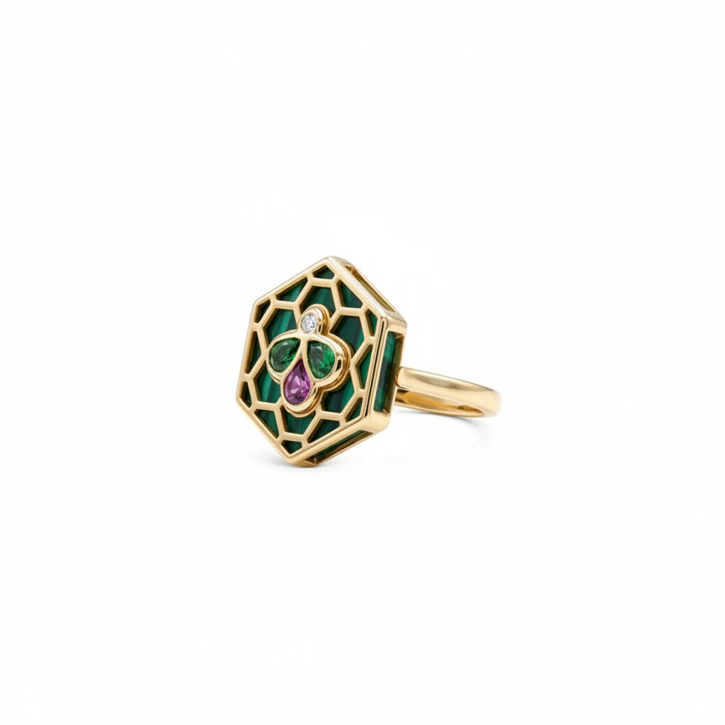 A gold hexagonal ring featuring green enamel inlay, a central green and purple clover motif, and a small clear gemstone, shown on a plain white background.