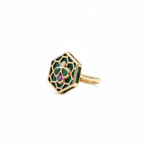 A gold hexagonal ring featuring green enamel inlay, a central green and purple clover motif, and a small clear gemstone, shown on a plain white background.