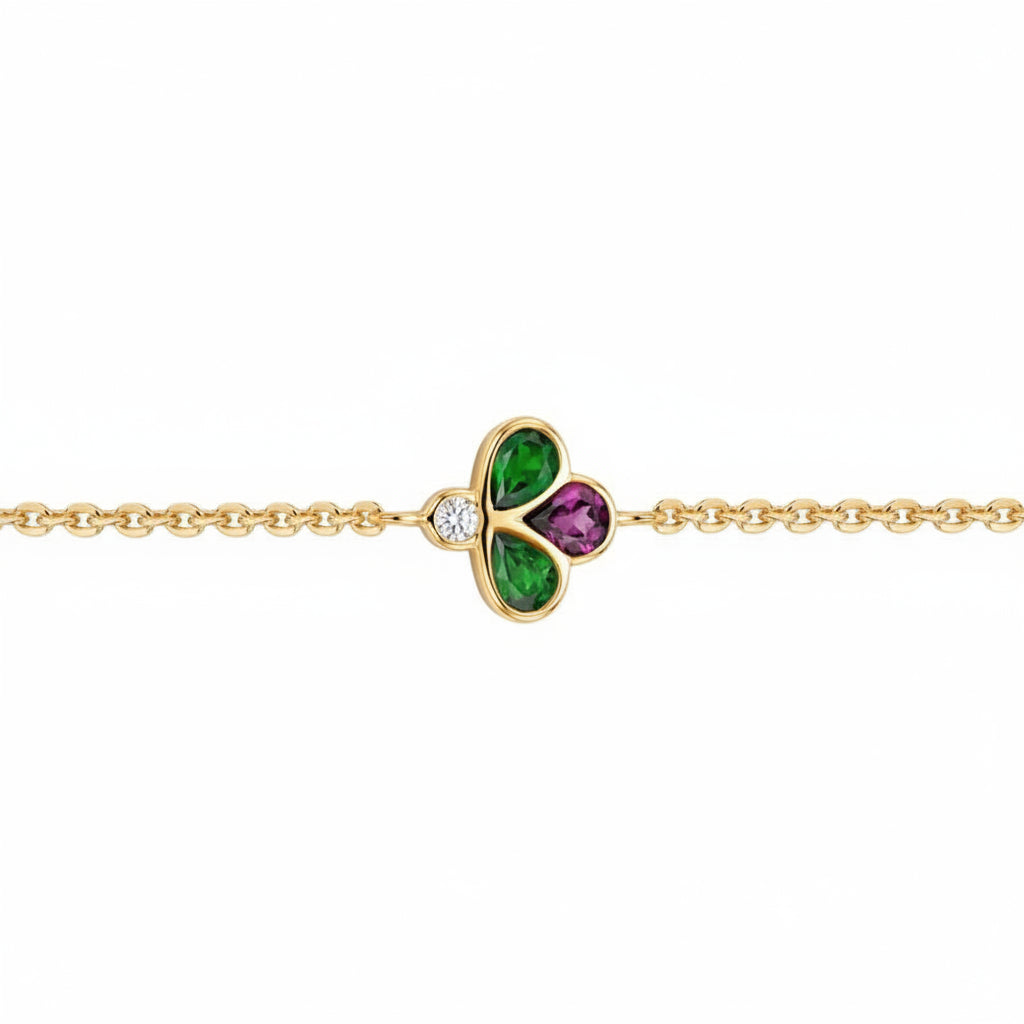 A gold chain bracelet featuring a central clover charm with green and purple stones, set against a plain white background.