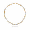 A yellow gold tennis necklace featuring multi-shaped diamonds in bezel settings, arranged in a circular shape on a white background with a soft reflection below.