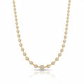 A yellow gold tennis necklace featuring a row of small bezel-set round spaced out diamonds with one larger central diamond at the center front, displayed on a clean white background with a soft reflection below.
