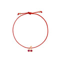 A red cord bracelet with an adjustable knot and a small rose gold-tone cherry charm featuring two pink gemstones, shown on a plain white background.

