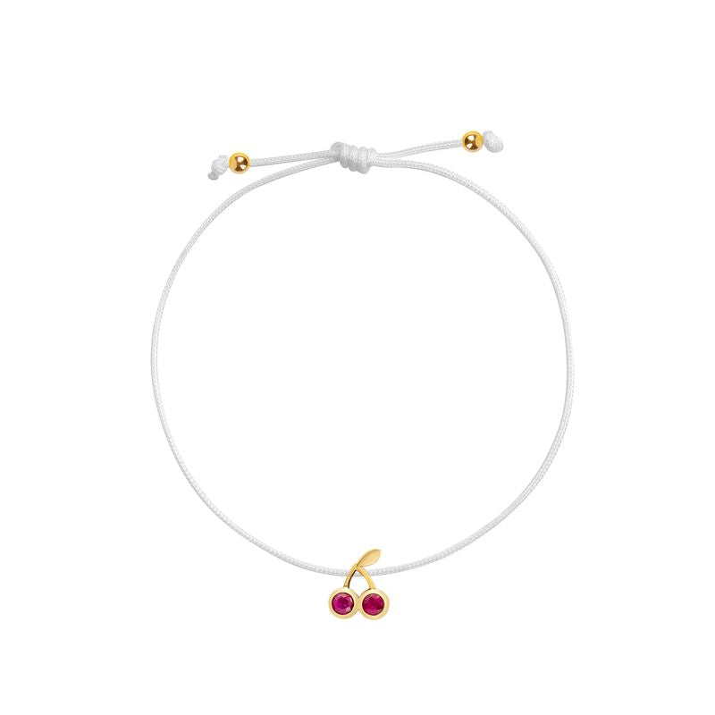 A delicate white cord bracelet featuring a small gold cherry charm with two red gemstone accents, displayed on a clean white background.