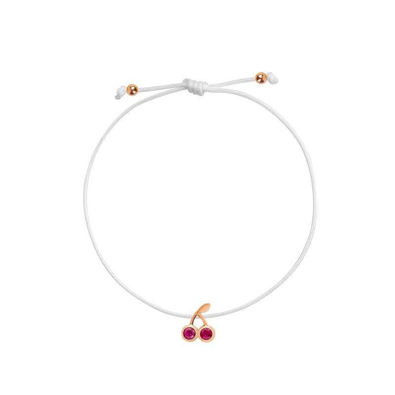 A delicate white cord bracelet featuring a cherry charm with two red gemstones and rose gold accents, shown on a plain white background.
