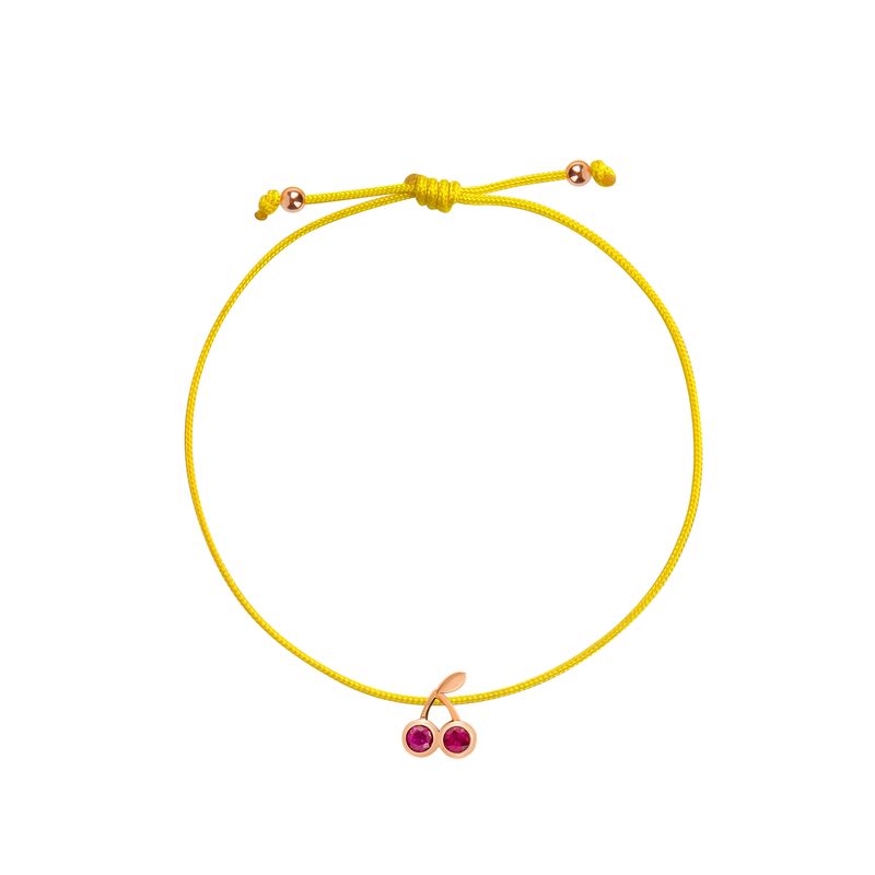 A yellow cord bracelet with a cherry charm featuring two red gemstones in a rose gold shown on a plain white background.