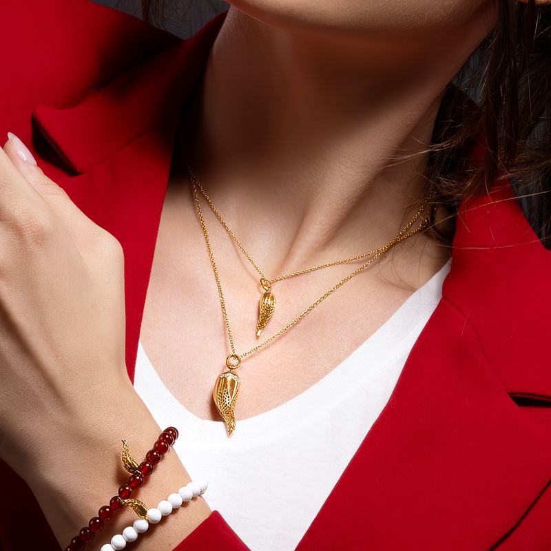 A close-up lifestyle shot of a woman wearing a double-layered gold necklace with matching horn pendants, styled with a red blazer, white shirt, and a beaded bracelet on her wrist.