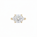 A yellow gold three-stone ring featuring a large cushion brilliant-cut center lab grown diamond flanked by two smaller trillion lab grown diamonds, set against a plain white background.

