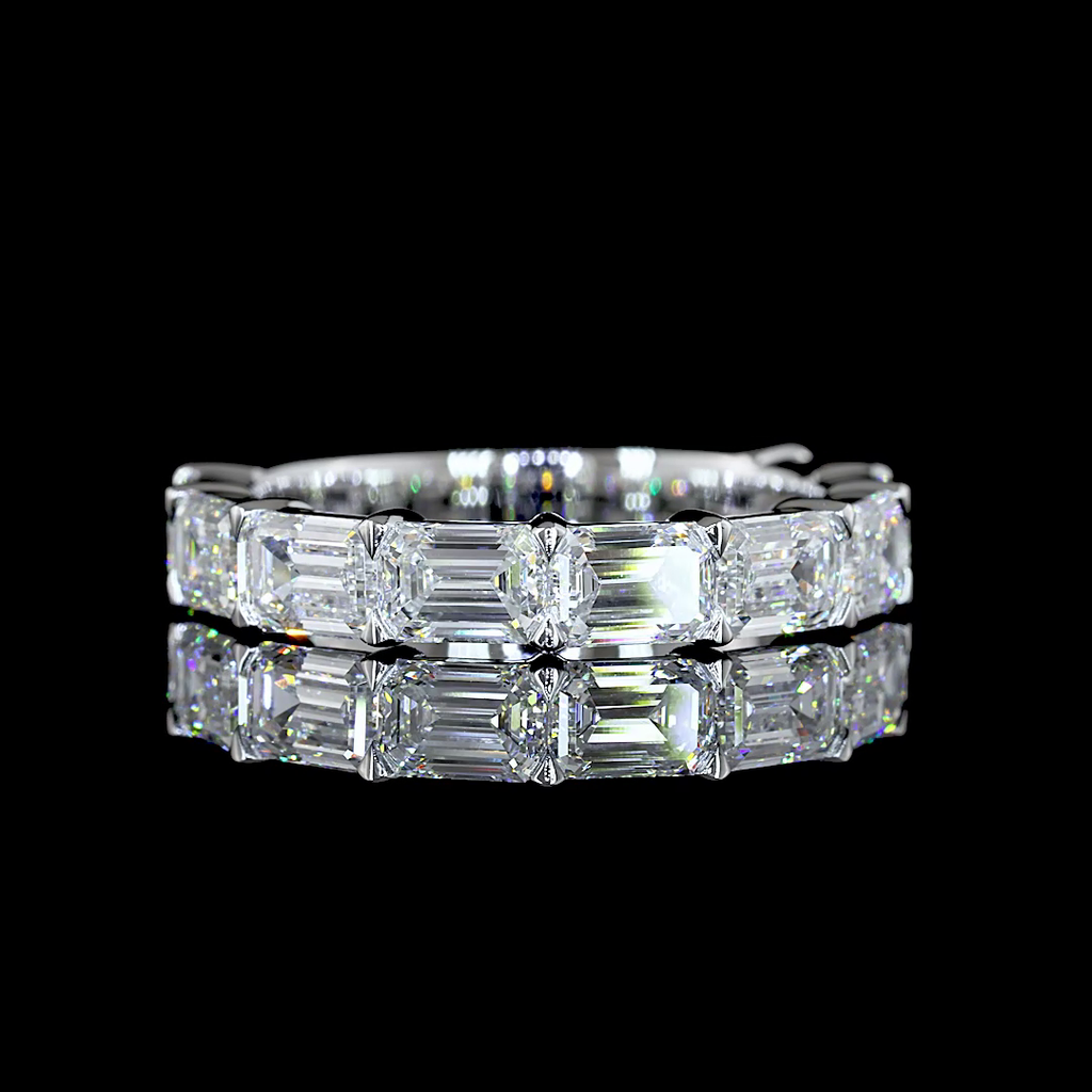 A white gold band ring featuring a row of lab grown emerald-cut diamonds, shown from a side profile on a clean black background. 3/4 all way around the band.