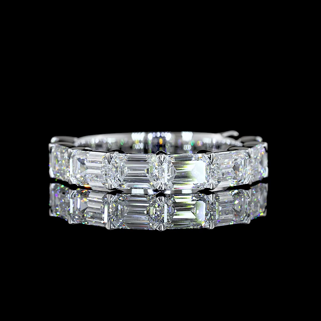 A white gold band ring featuring a row of lab grown emerald-cut diamonds, shown from a side profile on a clean black background. 3/4 all way around the band.
