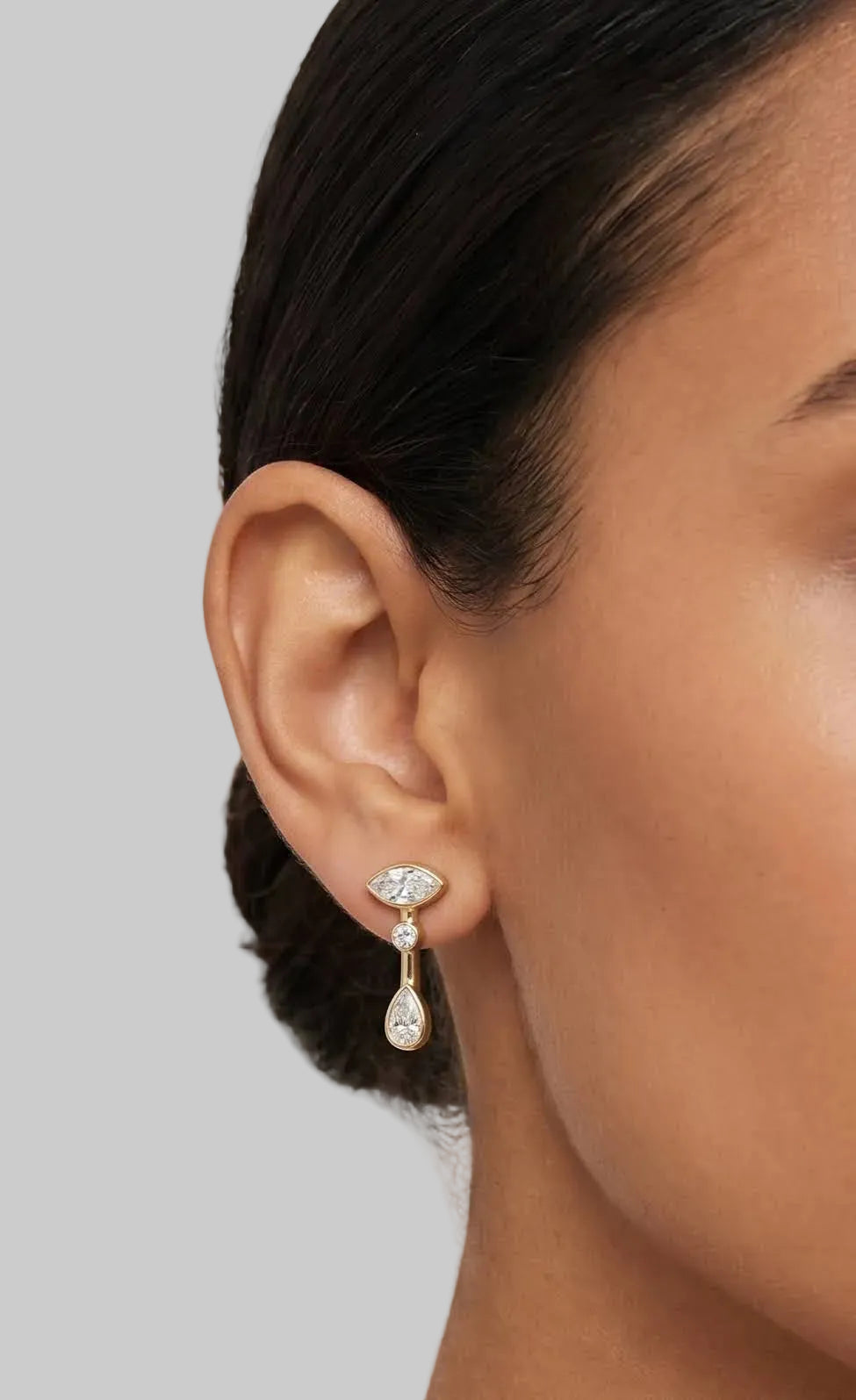 Pair of gold earrings with marquis, round and pear bezel set diamonds  on a model.
