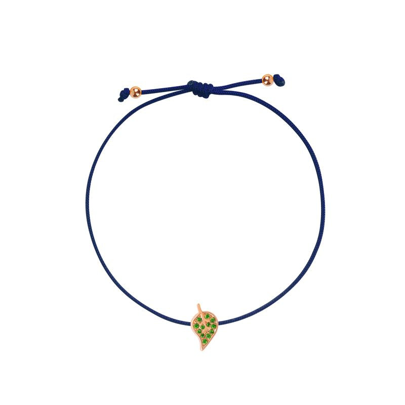 A delicate navy blue cord bracelet featuring a small leaf- shaped charm with green stones and a rose gold border, displayed on a clean white background.