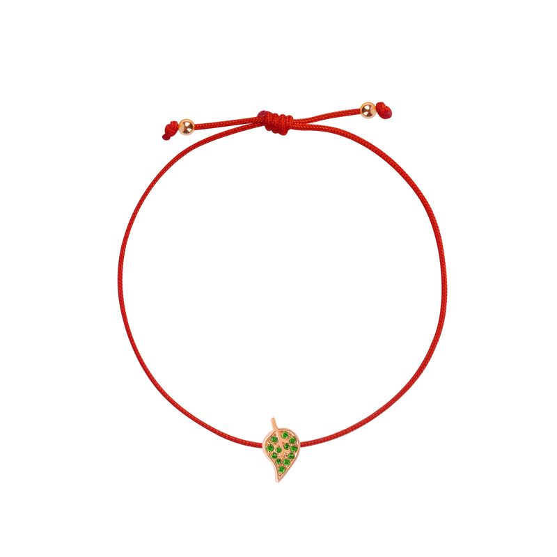 A delicate red cord bracelet featuring a small leaf- shaped charm with green stones and a rose gold border, displayed on a clean white background.