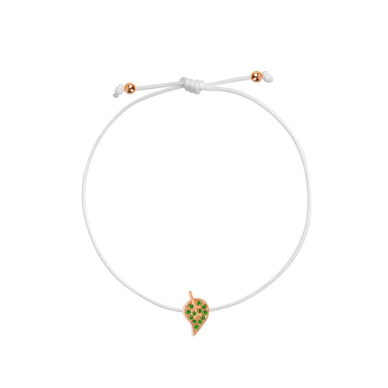 A delicate white cord bracelet featuring a small leaf- shaped charm with green stones and a rose gold border, displayed on a clean white background.