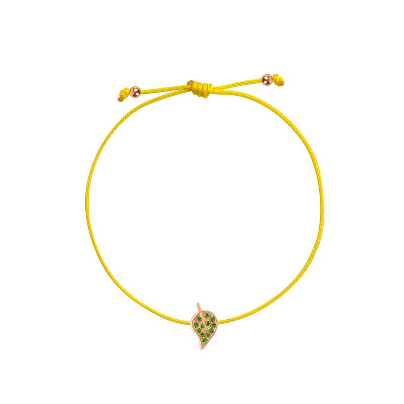 A delicate yellow cord bracelet featuring a small leaf- shaped charm with green stones and a rose gold border, displayed on a clean white background.