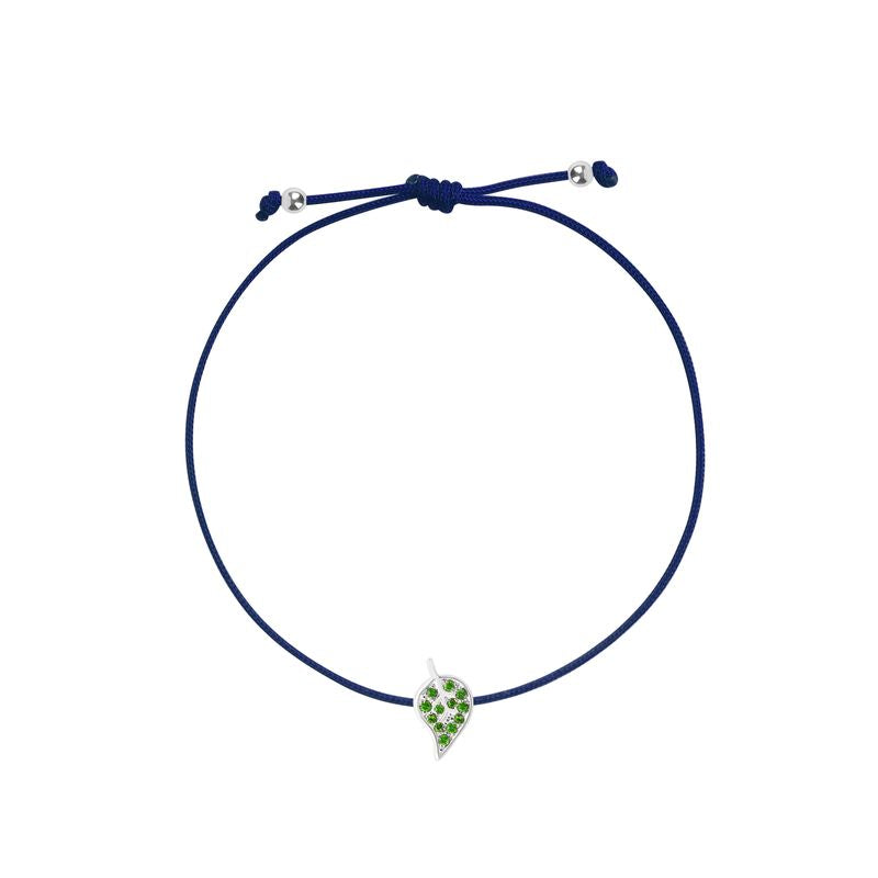 A navy blue cord bracelet featuring a small white gold leaf charm embellished with green stones, displayed on a clean white background.