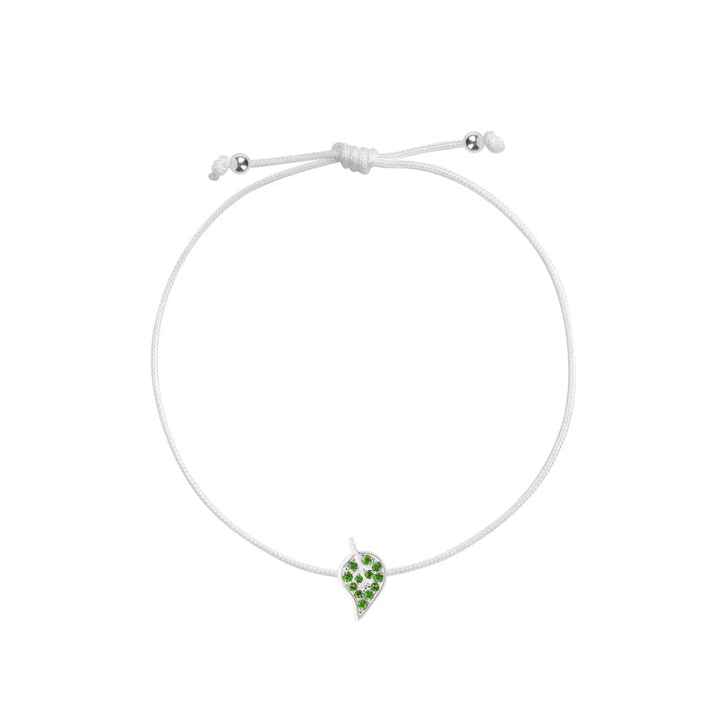 A white cord bracelet featuring a small white gold leaf charm embellished with green stones, displayed on a clean white background.