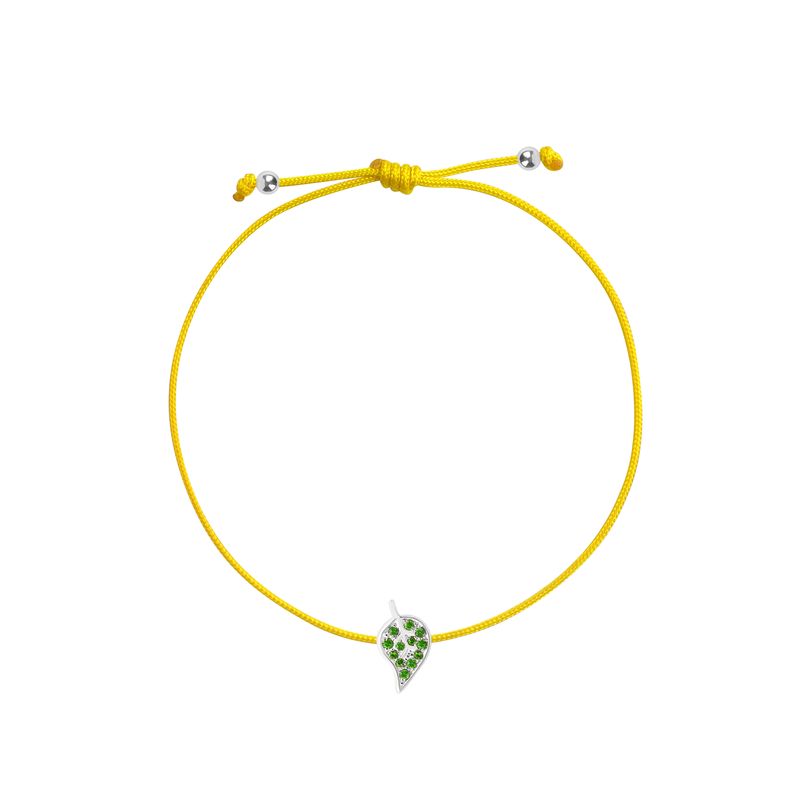 A yellow cord bracelet featuring a small white gold leaf charm embellished with green stones, displayed on a clean white background.
