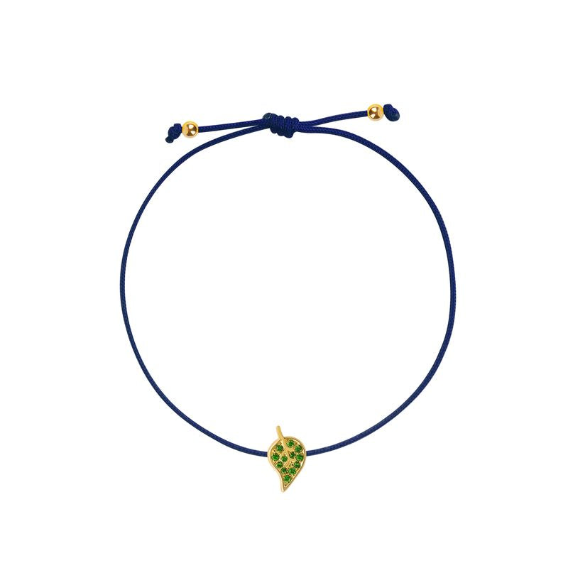 A navy blue  cord bracelet featuring a small yellow gold leaf charm embellished with green stones, displayed on a clean white background.