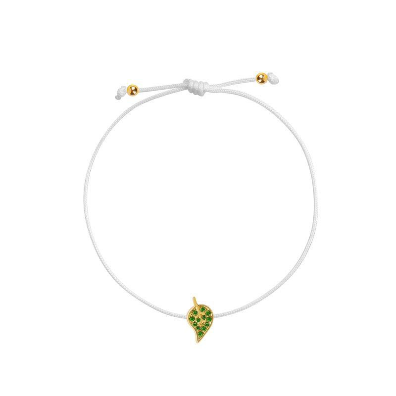 An white cord bracelet featuring a small yellow gold leaf charm embellished with green stones, displayed on a clean white background.