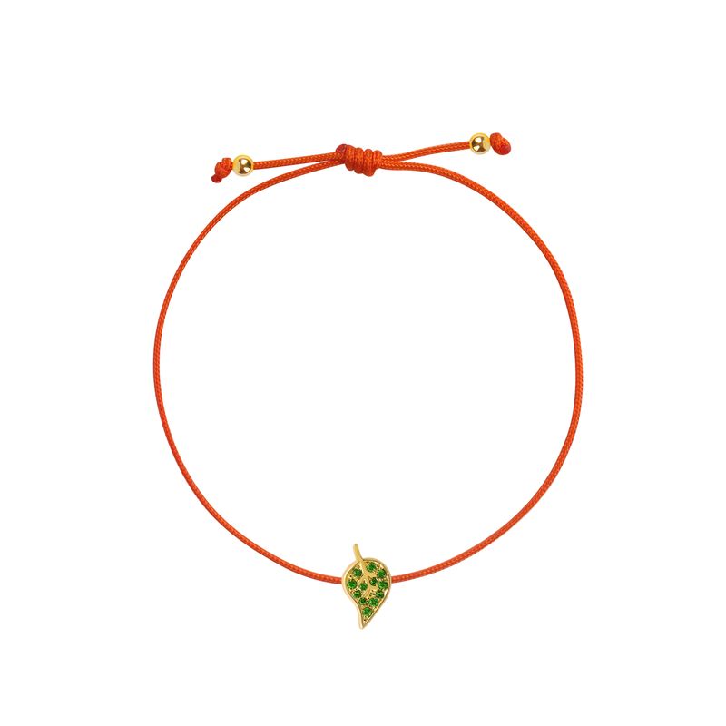An orange cord bracelet featuring a small yellow gold leaf charm embellished with green stones, displayed on a clean white background.
