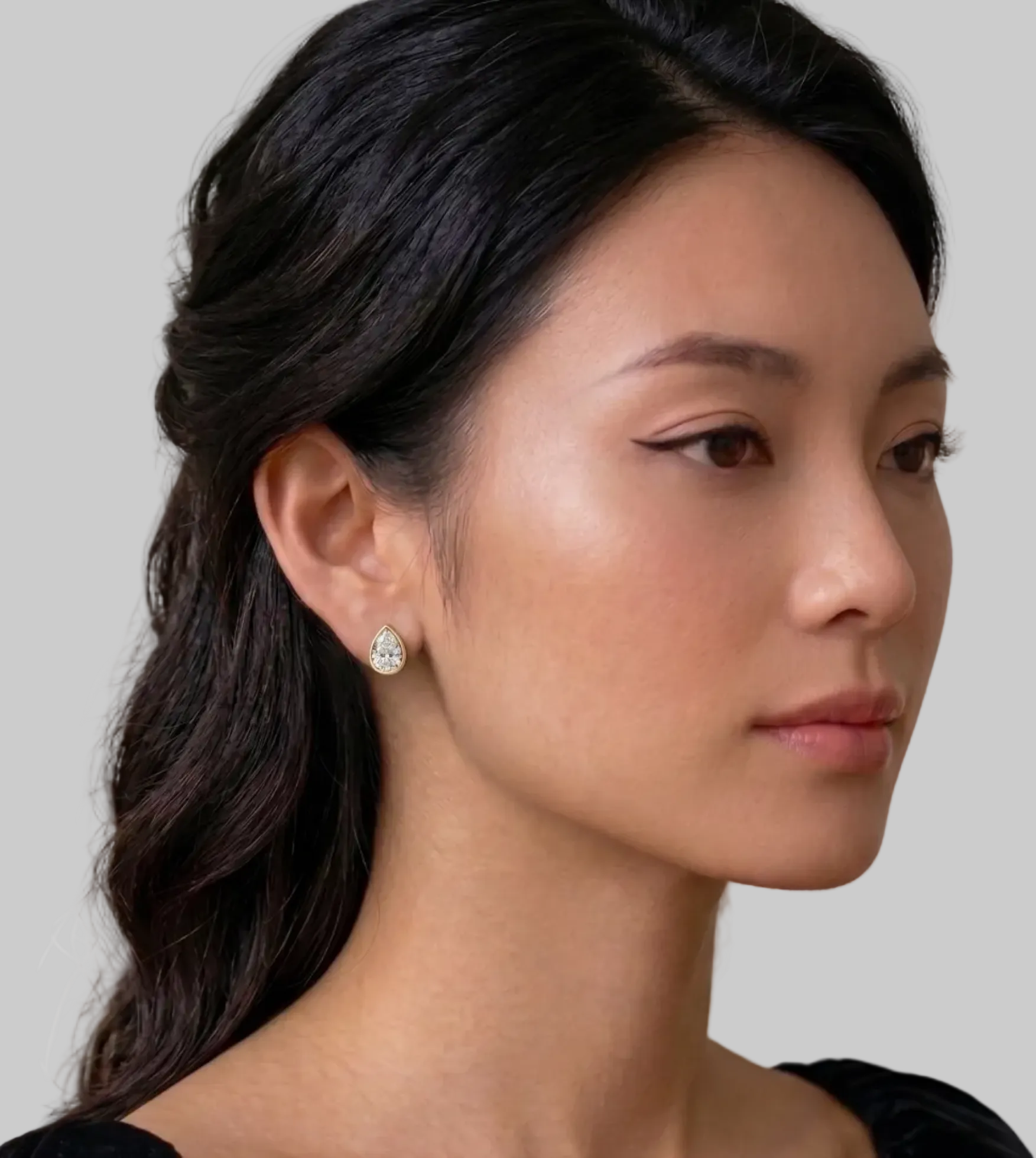 A pair of pear-shaped diamond bezel set stud earrings in yellow gold, shown on a model.
