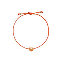 An orange adjustable cord bracelet with a small rose gold apple-shaped charm in the center, displayed on a clean white background.