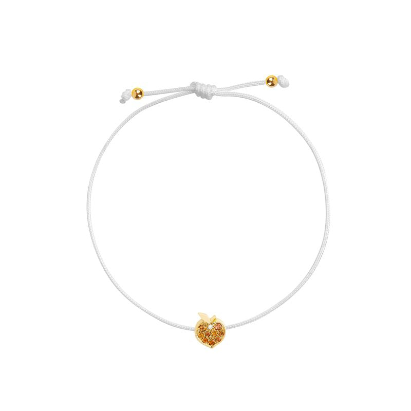 A white cord bracelet featuring a small gold peach-shaped charm adorned with tiny orange stones, presented on a solid white background.