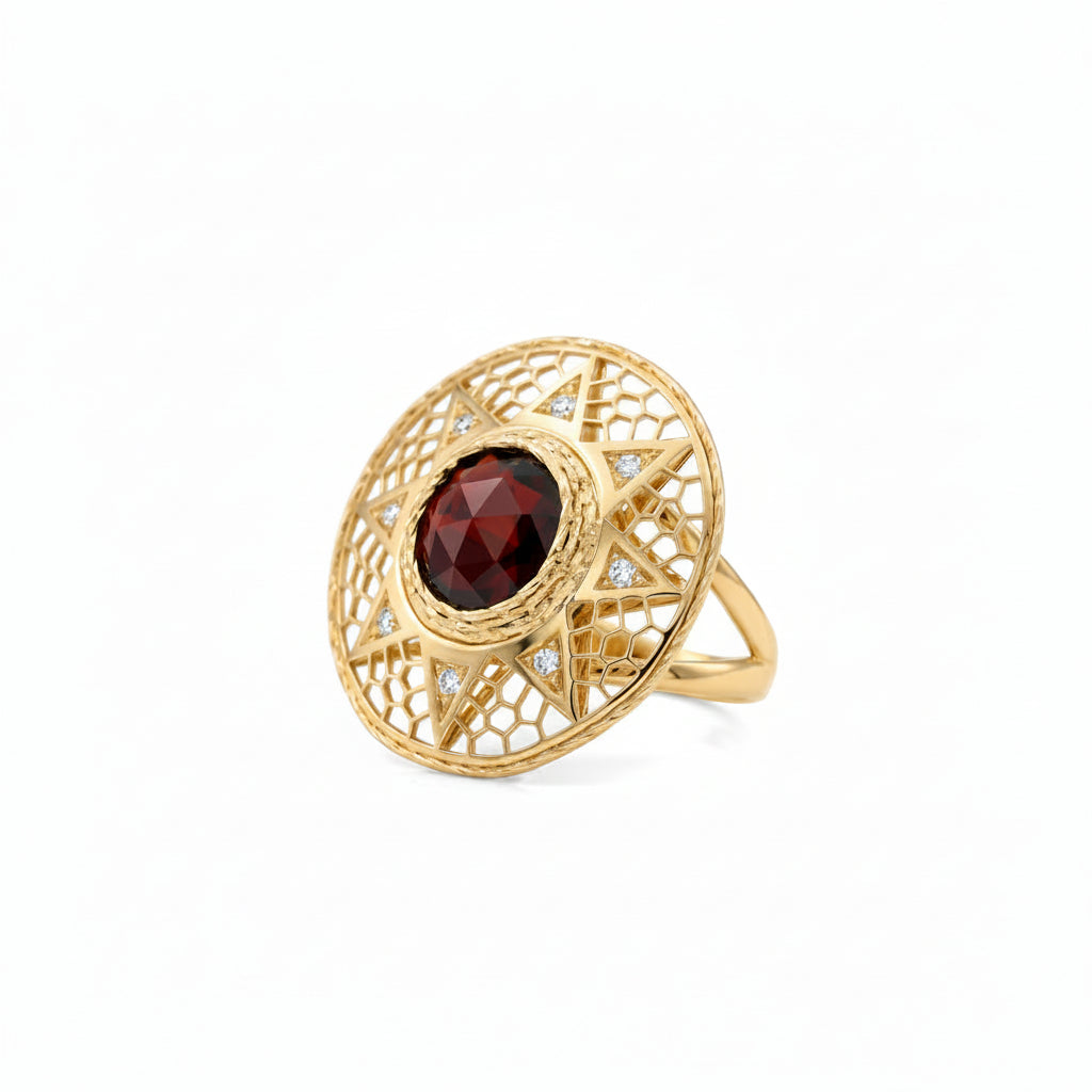 A gold filigree ring featuring a large round  faceted dark red garnet in the center, with small clear stones set along the inner circular frame, shown on a plain white background.