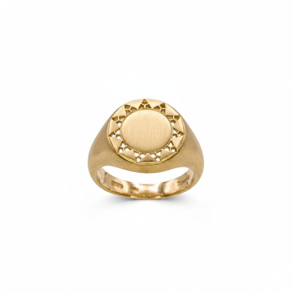 A yellow gold signet ring with a circular sunburst design on the face, featuring a brushed center and small cutout details around the border, shown on a plain white background.