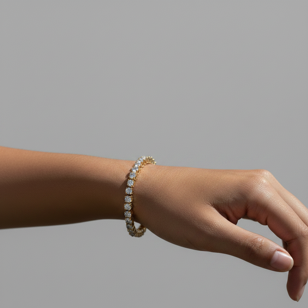 Close-up view of four-prong round lab grown diamonds set in 14k yellow gold tennis bracelet link. A close-up of a person's wrist wearing a delicate gold tennis bracelet with diamonds shown on the light gray background.