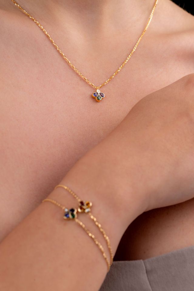 A close-up lifestyle shot of a model wearing a delicate gold chain necklace and a matching gold double-strand bracelet, both featuring small clover charms.