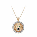A round lion head pendant necklace in yellow gold with a halo of small white diamonds around the border and green gemstone eyes, suspended from a delicate gold chain on a white background.