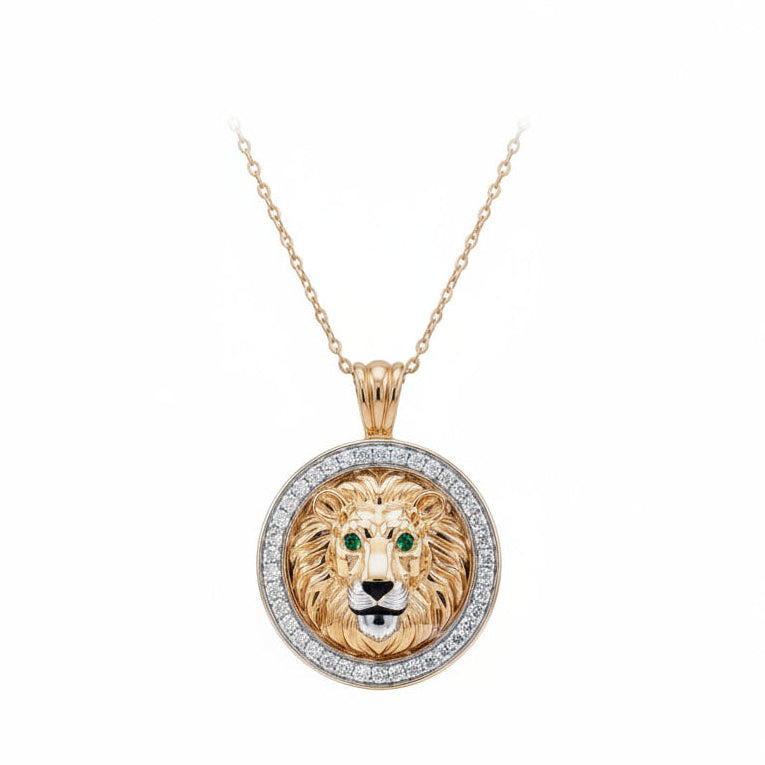 A round lion head pendant necklace in yellow gold with a halo of small white diamonds around the border and green gemstone eyes, suspended from a delicate gold chain on a white background.