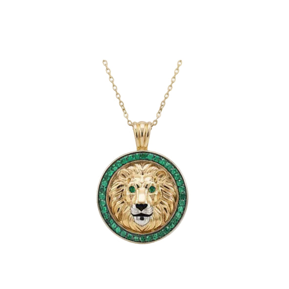 A gold lion pendant necklace featuring a detailed lion face with green emerald gemstone eyes and a border of green emerald stones, suspended from a delicate gold chain against a white background.