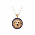 A gold lion pendant necklace featuring a detailed lion head in the center, surrounded by a halo of small blue sapphire stones, suspended from a delicate gold chain against a plain white background.