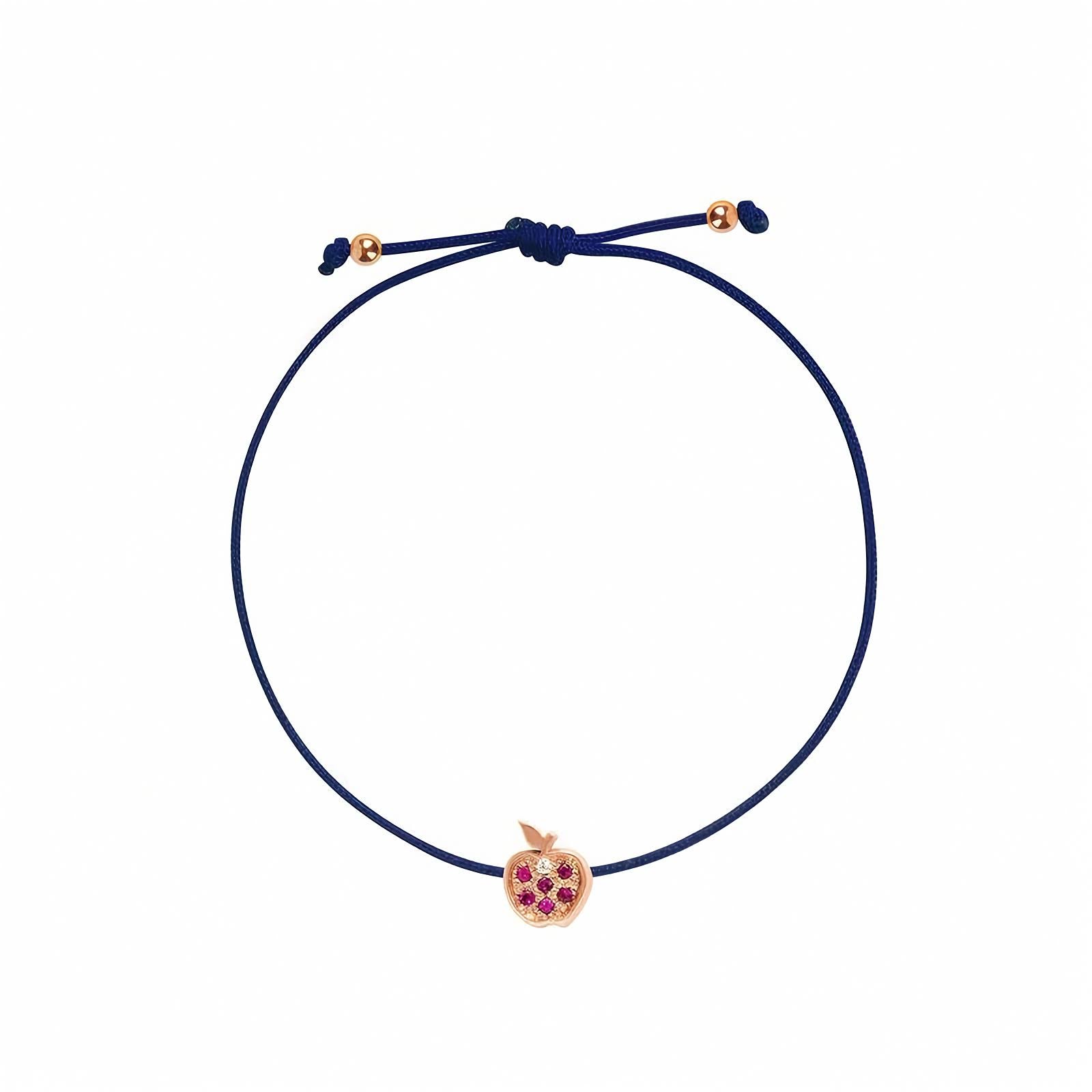 Rosmundo collaboration 18k rose gold apple string bracelet with natural rubies and diamond on adjustable macrame cord. A navy blue cord bracelet with a small rose gold apple charm set with purple gemstones, shown on a plain white background.