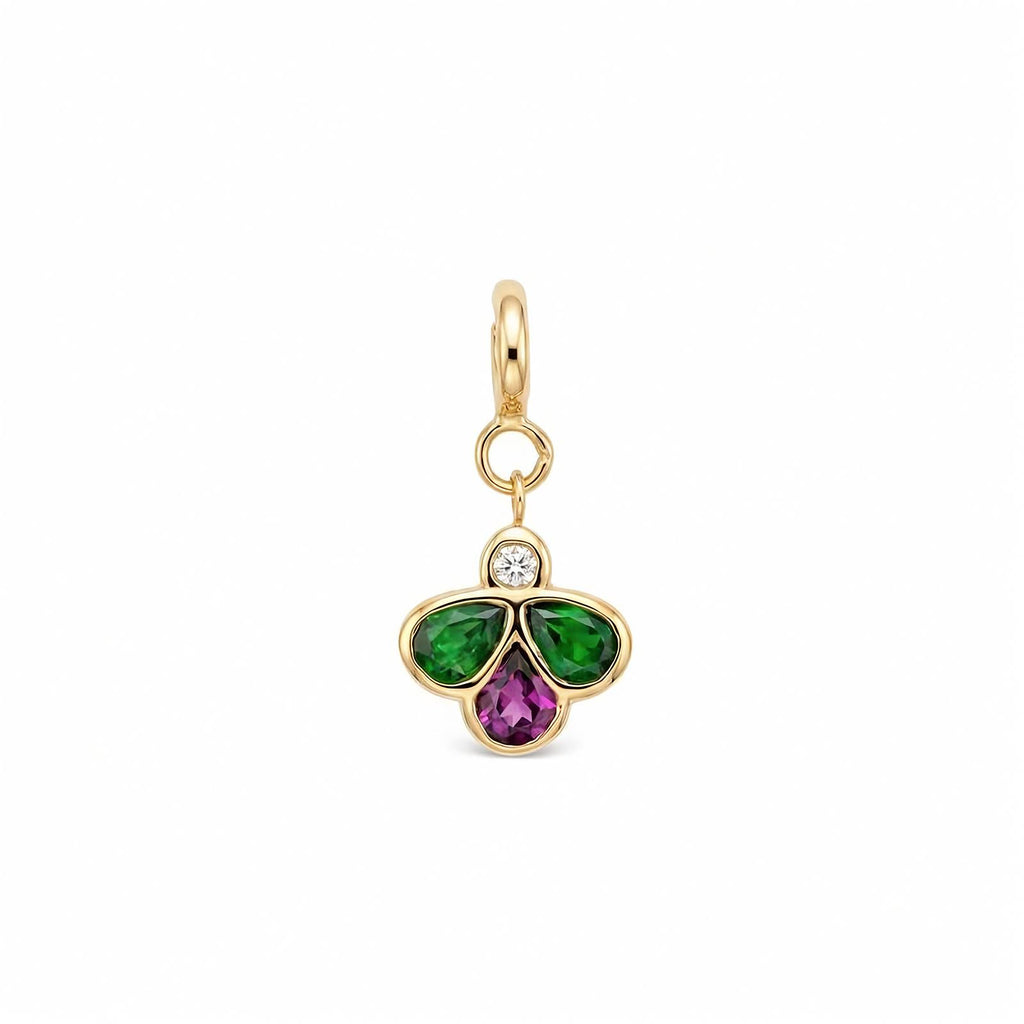 A yellow gold charm pendant featuring a three-petal bee design with a green gemstones on the left and right, a purple pear-cut stone in the center, and a small clear round-cut diamond at the top, set in a polished gold bezel with a hanging loop.