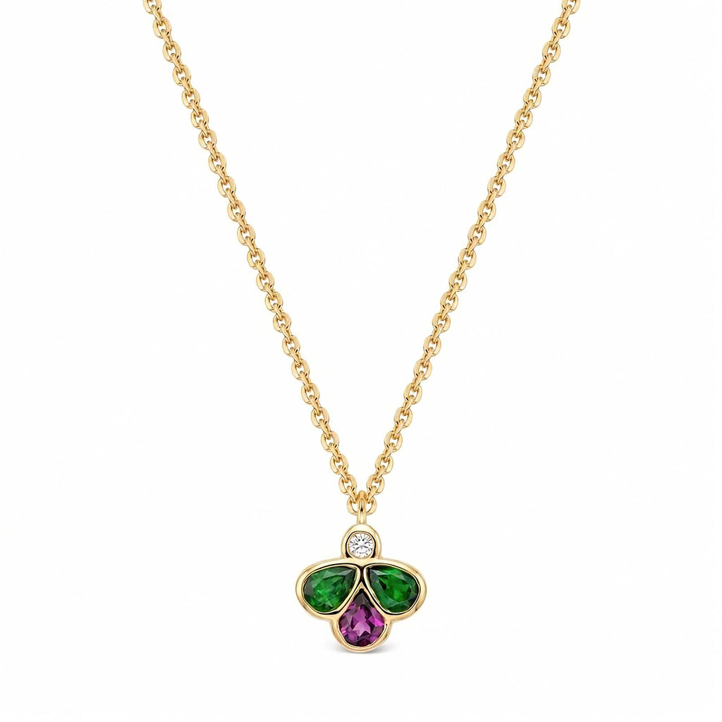 A gold chain necklace with a clover-shaped pendant featuring a small round diamond at the top, a green teardrop-shaped stones on the left and right, and a purple teardrop-shaped stone in the middle, set against a plain white background.