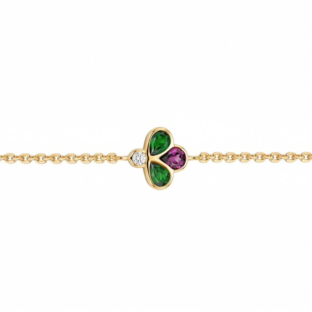 A gold chain bracelet featuring a central clover charm with green and purple stones, set against a plain white background.