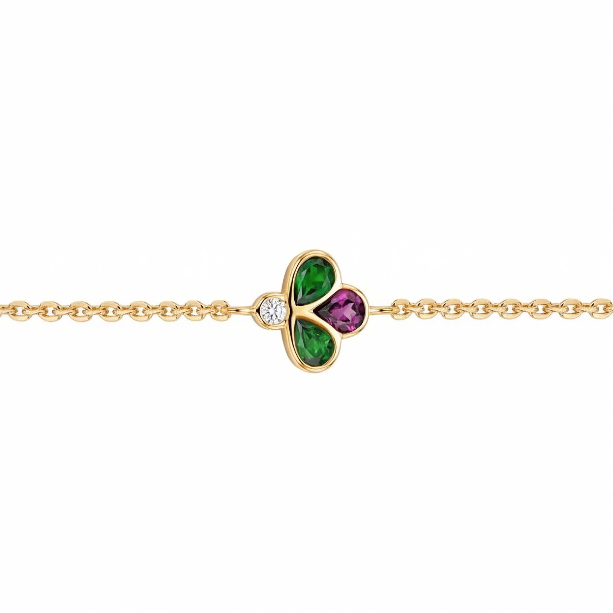 A gold chain bracelet featuring a central clover charm with green and purple stones, set against a plain white background.