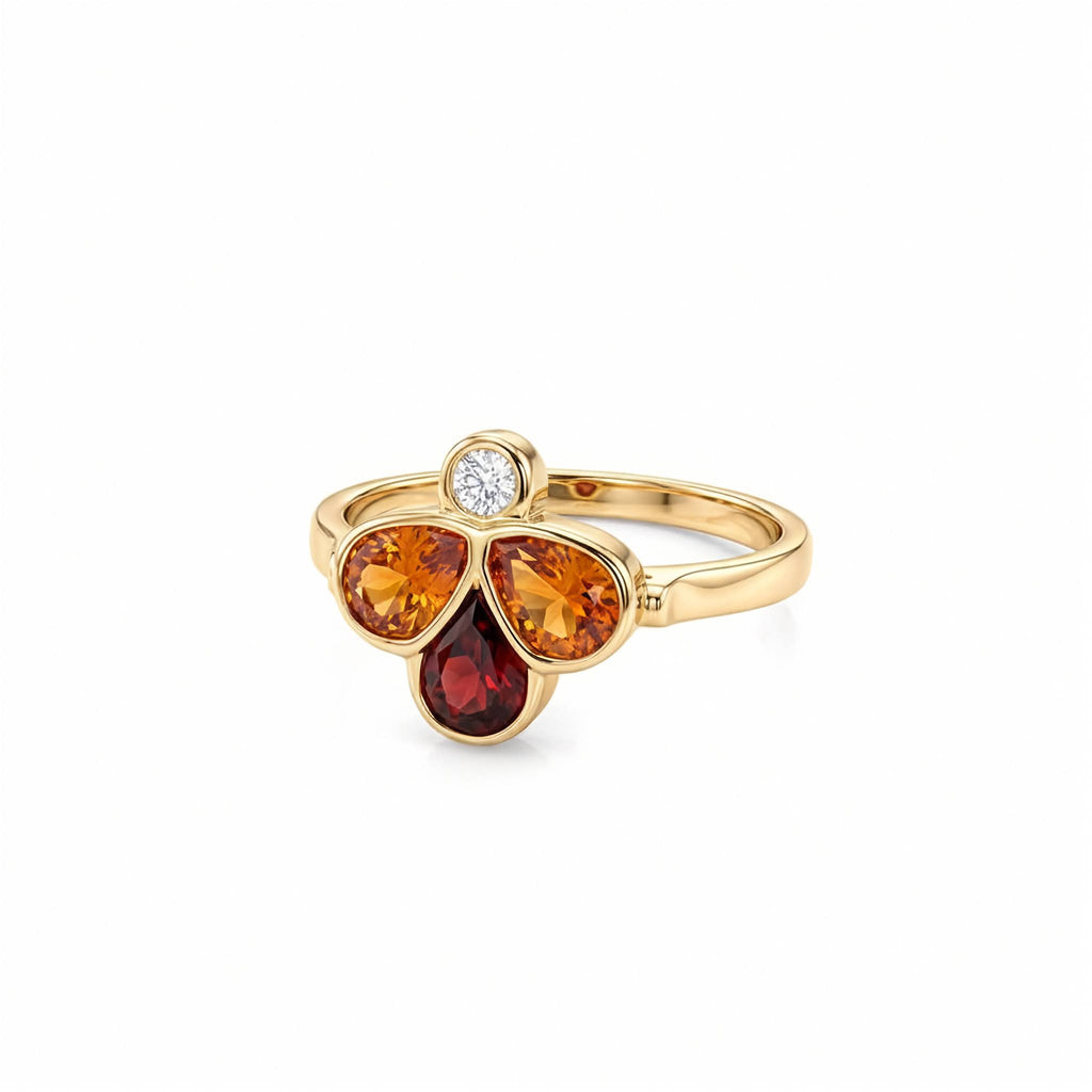 A yellow gold ring featuring three gemstone clusters: a top round white diamond, a middle pear-cut two orange stone, and a bottom teardrop-cut dark red stone, set on a polished gold band against a white background.