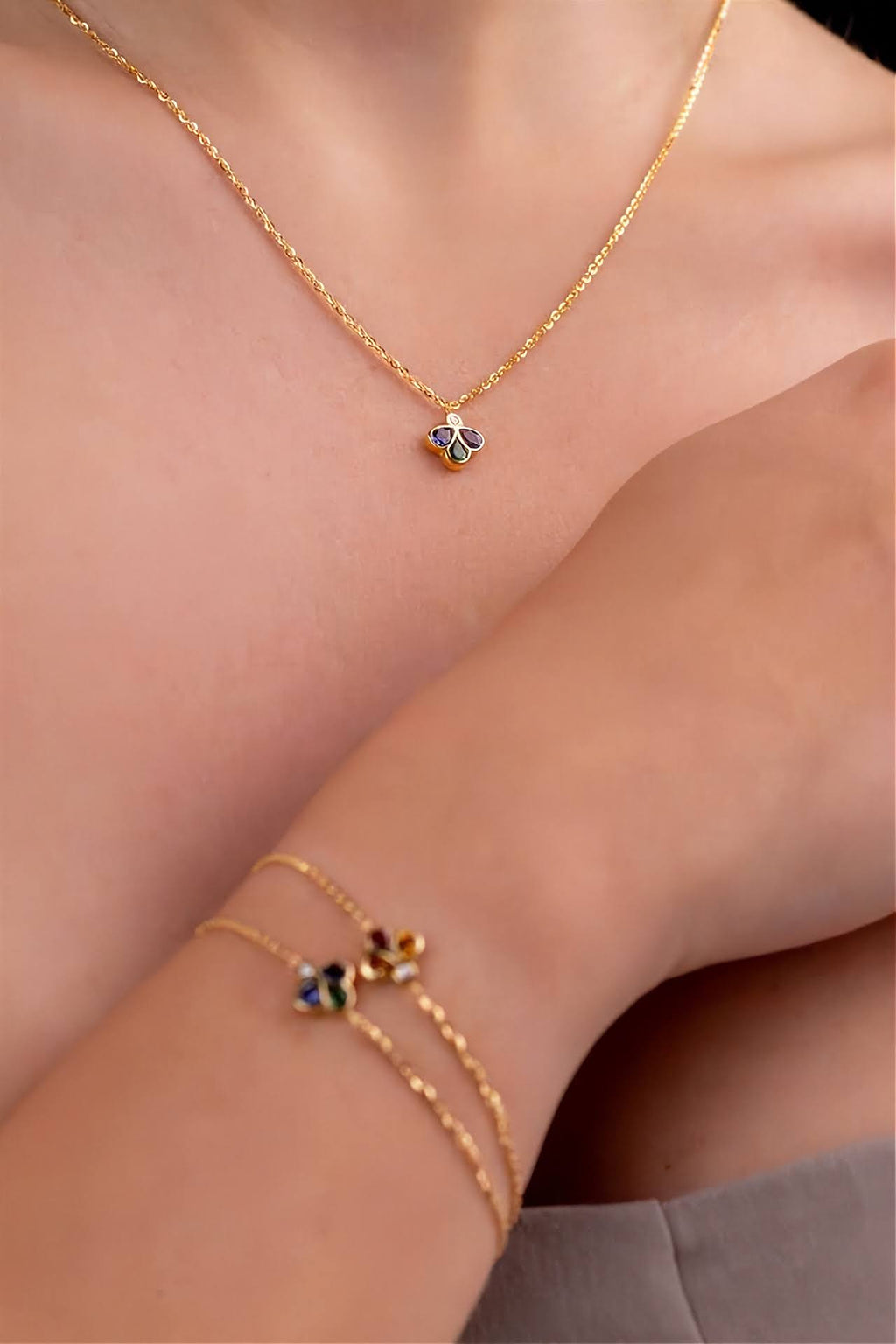 A close-up lifestyle shot of a model wearing a delicate gold chain necklace and a matching gold double-strand bracelet, both featuring small clover charms.